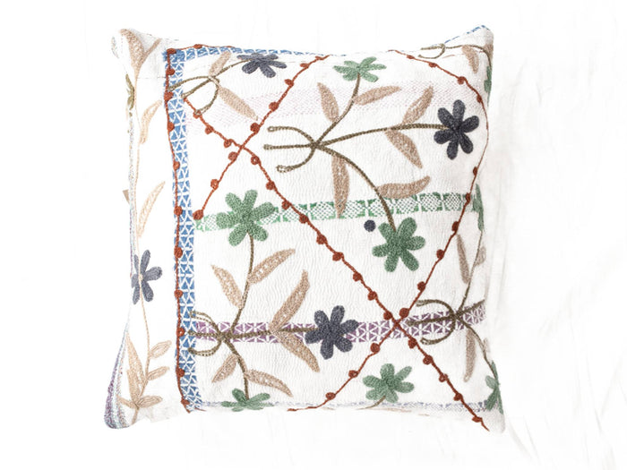 Suzani Kissenbezug 50x50 cm in Weiß mit farbenfrohen, gestickten Blumen in Grün, Blau und Grau sowie orangefarbenen Umrissen und Fransen für einen Boho-Vintage-Stil.